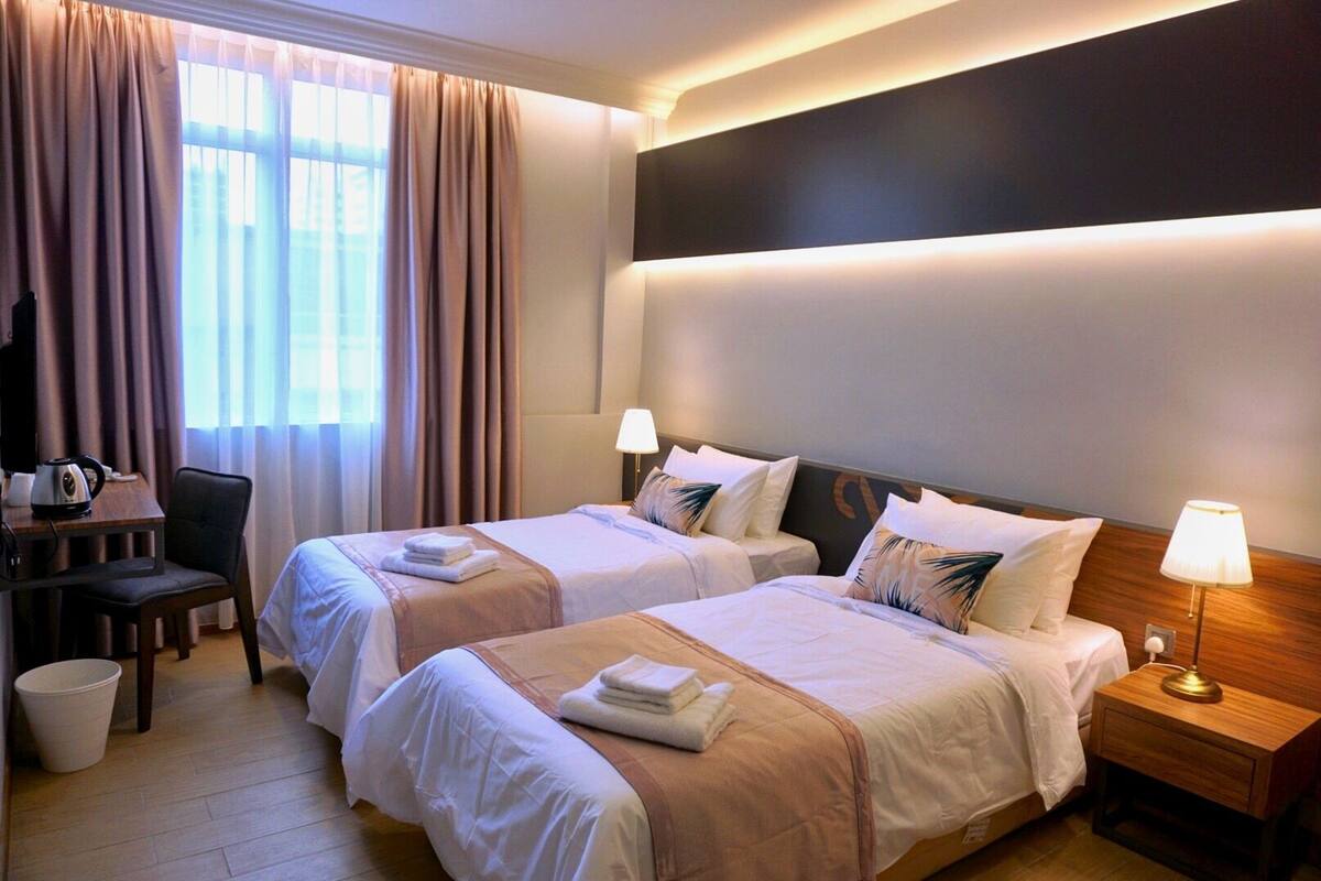 A hotel room with two beds, a desk with a chair, a TV, and a lamp.
