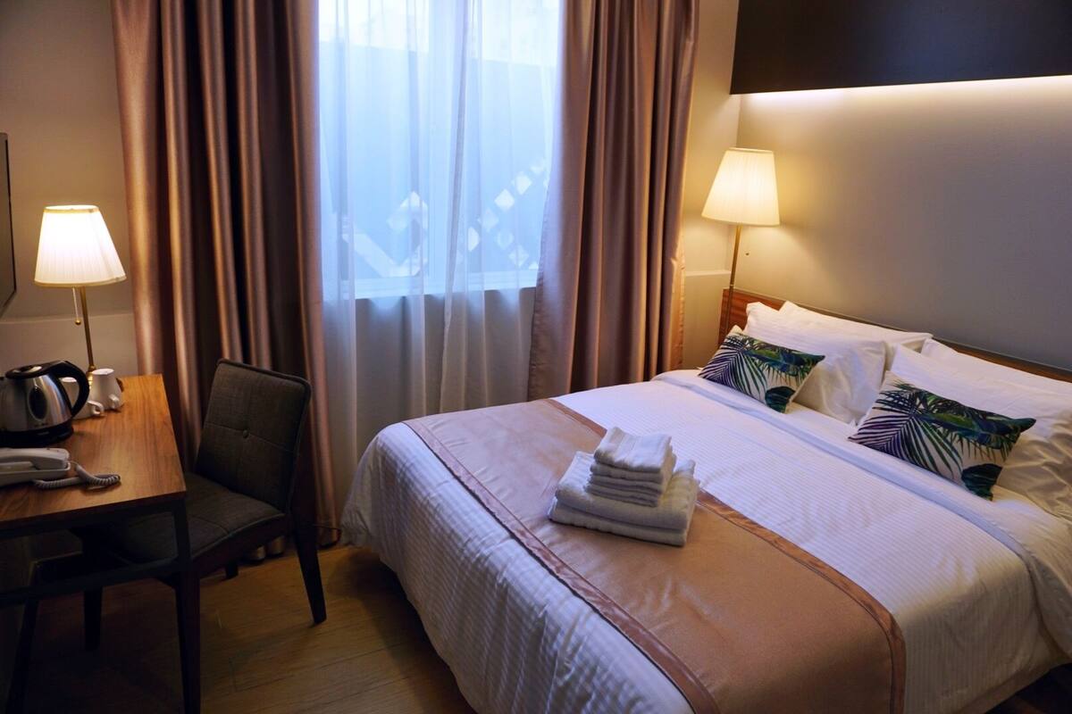 A hotel room with a neatly made bed, a desk with a lamp, a telephone, and a chair.