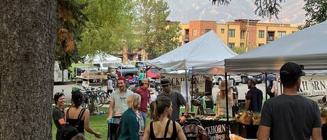 A market scene with people and tents, surrounded by trees and buildings in the background.