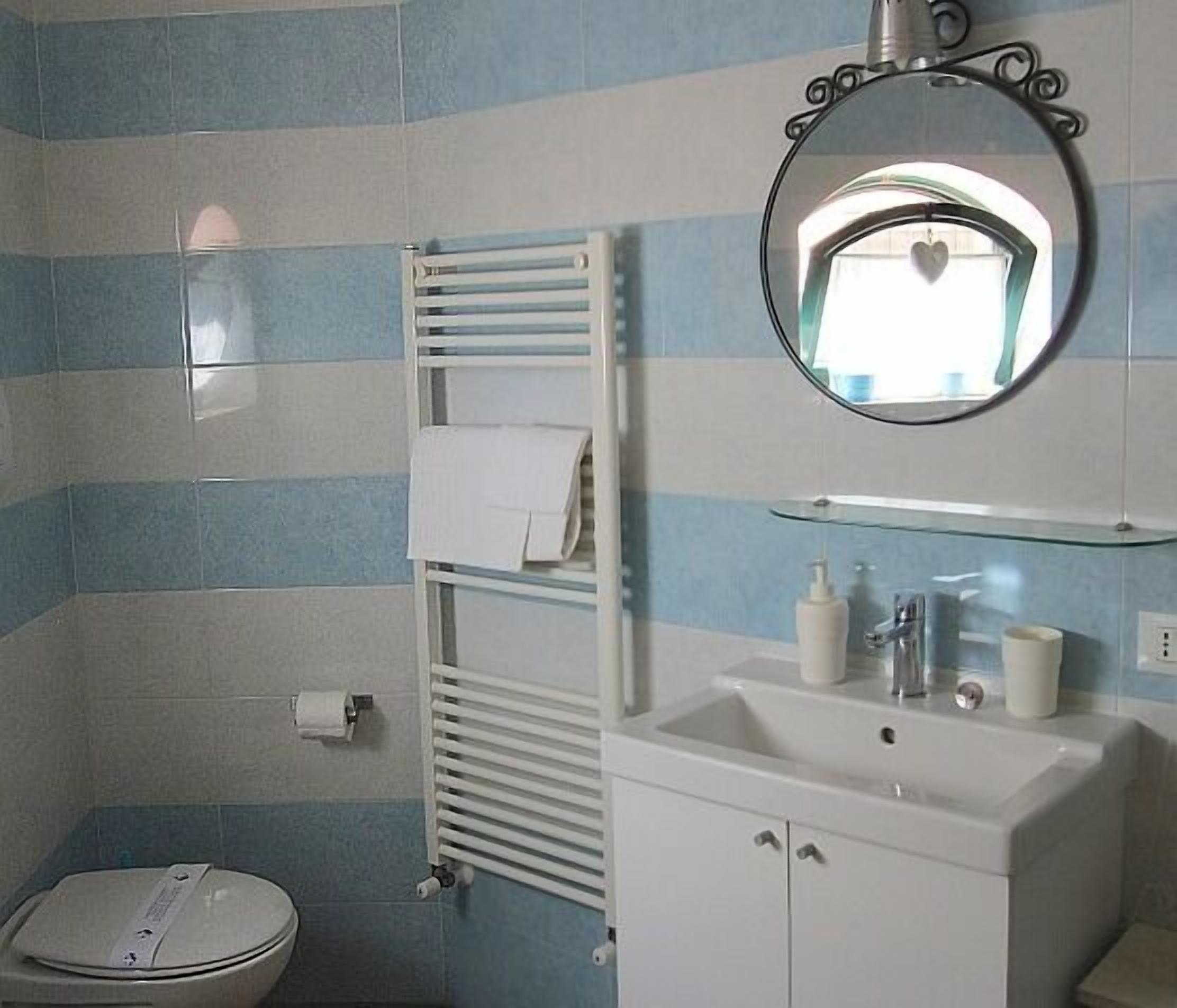 Une salle de bain avec un mur recouvert de carreaux à rayures, un lavabo blanc avec un miroir au-dessus, un porte-serviettes et des toilettes.