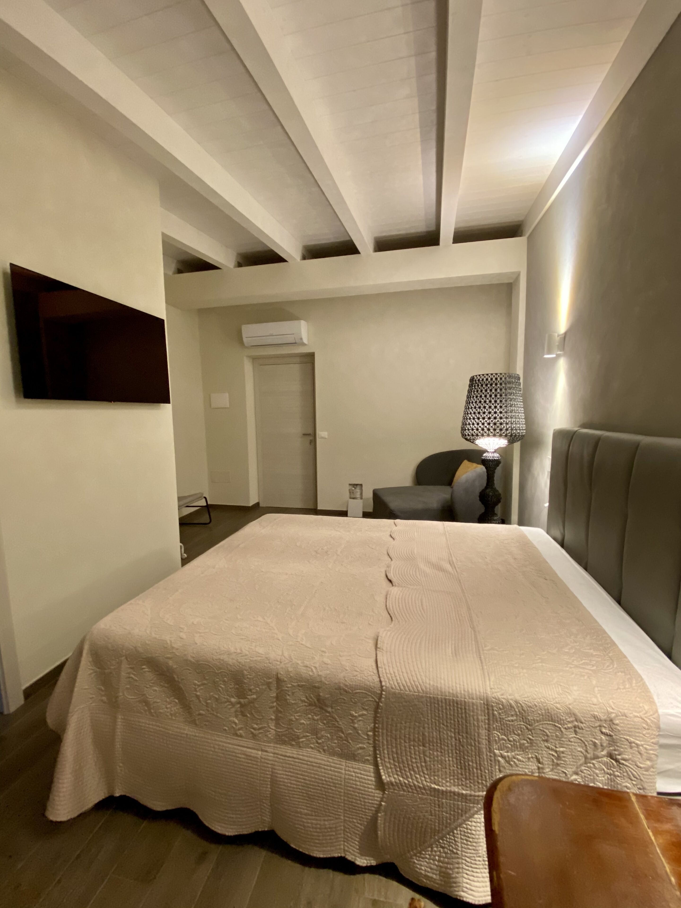 Ein Schlafzimmer mit einem großen Bett, einem an der Wand montierten Fernseher, einer Nachttischlampe und einer Klimaanlage.