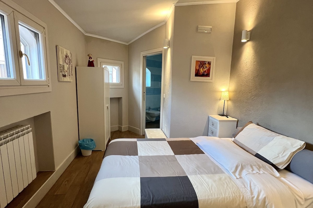 A bedroom with a large bed, a radiator, a window, and a door leading to another room.