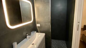 Un baño moderno con un espejo grande, un lavabo blanco y una zona de ducha.