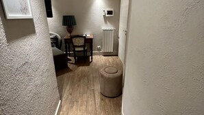 A narrow hallway with wooden flooring, a small round ottoman, a table with chairs, a lamp, and a radiator. - Hotel Bella Napoli (Foggia)
