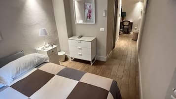 A hotel room with a bed, bedside table, lamp, dresser, and an air conditioning unit.