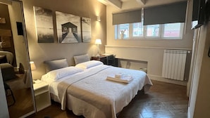 A bedroom with a large bed, a bedside table with a lamp, a window with blinds, and a radiator. - Hotel Bella Napoli (Foggia)
