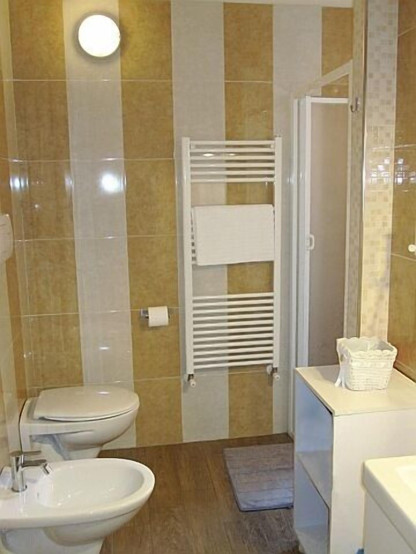 Une salle de bain équipée d’un WC, d’un bidet, d’un lavabo, d’un porte-serviettes et d’un panier posé sur le comptoir.