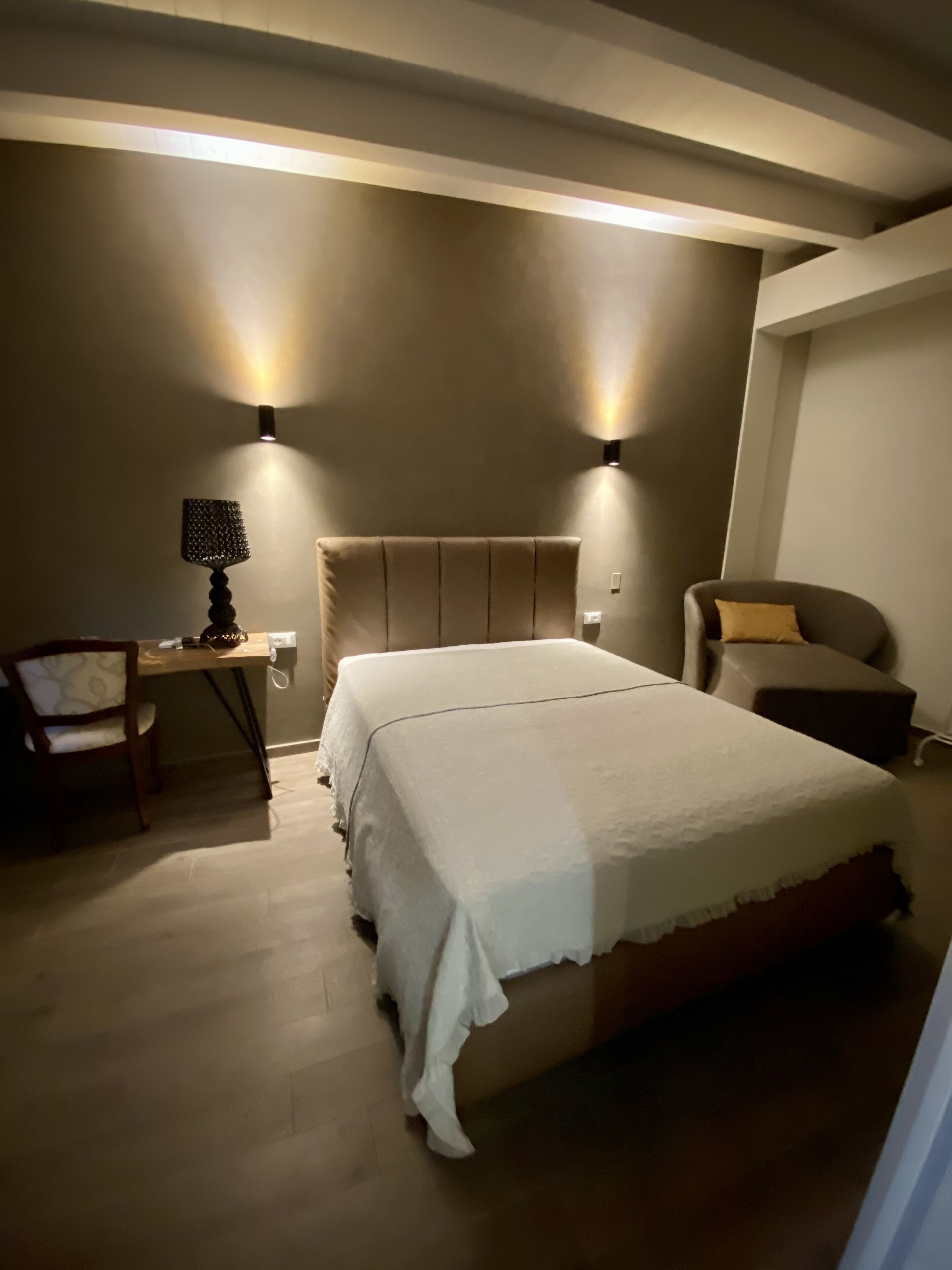 Un dormitorio con cama, un escritorio, una silla y dos lámparas fijadas a la pared.