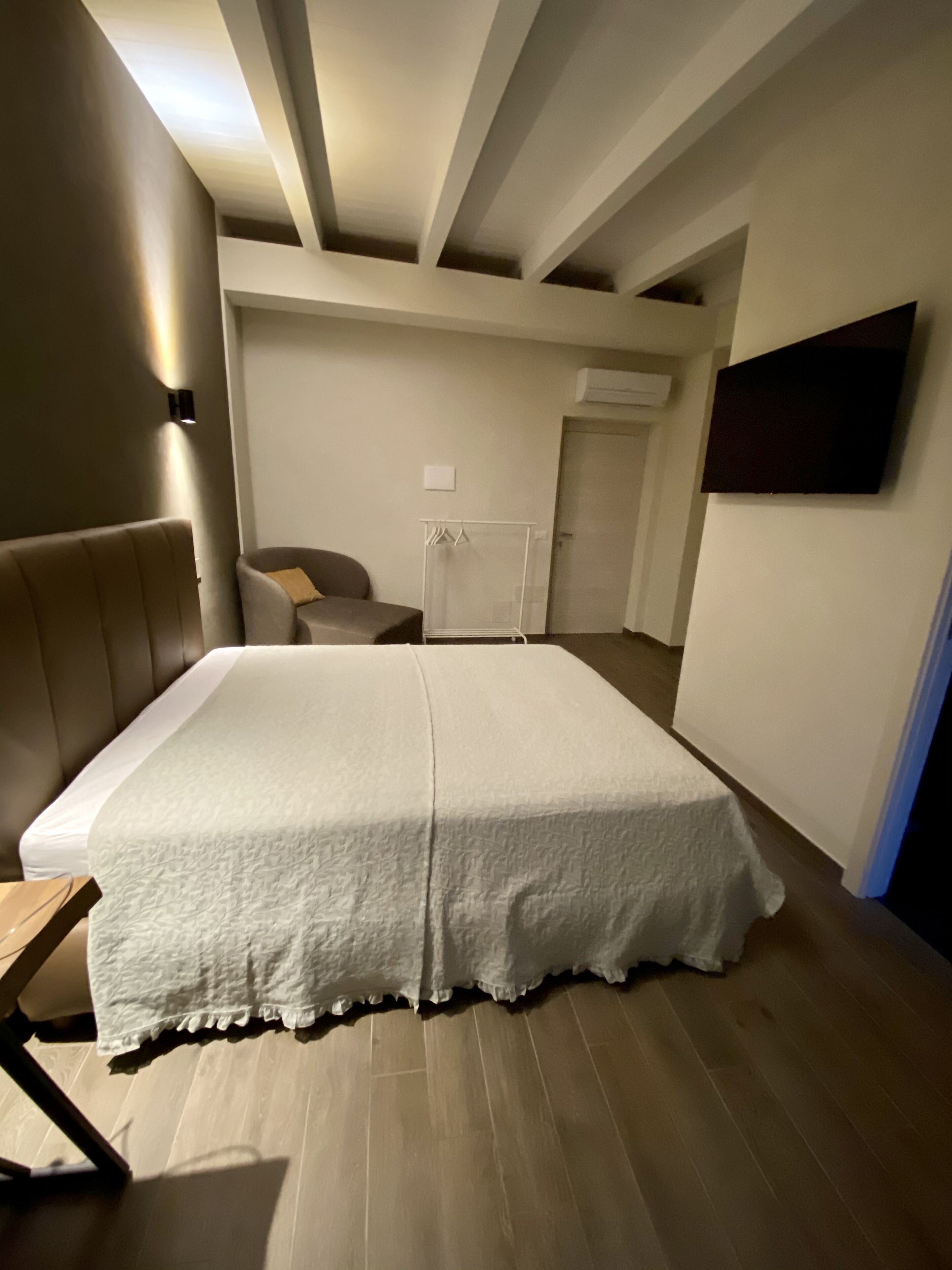 A bedroom with a bed, a chair, a small table, and a TV mounted on the wall.