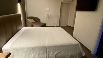 A bedroom with a bed, a chair, a small table, and a TV mounted on the wall.