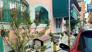 A red car parked on a street with a building featuring a green awning and a window with a wreath decoration. - Hotel Bella Napoli (Foggia)