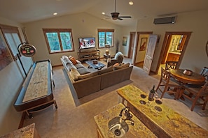 A spacious living room with a pool table, a sofa, a television, and a dining area with a wooden table and chairs.