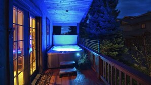 Un jacuzzi en una terraza de madera con vistas a árboles y una casa al fondo.
