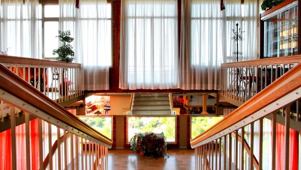 A grand staircase with a wooden railing, leading to a lower level with a view of greenery outside. - Amelia Dream View (Marliana)