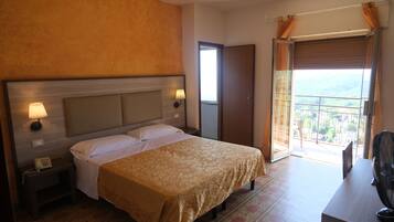 Una camera d'albergo con un letto, una lampada da comodino, un telefono e un balcone con vista.