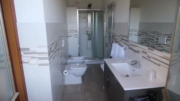 A modern bathroom with a glass-enclosed shower, a toilet, a bidet, and a sink.