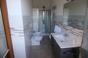 Un baño moderno con ducha envuelta en vidrio, inodoro, bidé y lavamanos.