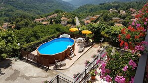 A swimming pool with a wooden deck, surrounded by a fence, and overlooking a valley with houses and greenery. - Amelia Dream View (Marliana)