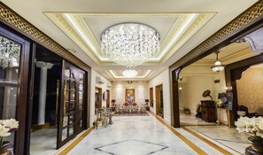A grand hallway with a marble floor, a large chandelier, and ornate wall decorations. - Grand Uniara (Jaipur)