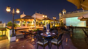 Un área de comedor al aire libre con mesas, sillas, sombrillas e iluminación decorativa.
