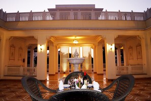 An indoor dining area with a table set for two, a decorative fountain, and ornate architectural details. - Grand Uniara (Jaipur)