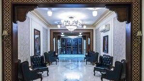 Un vestíbulo espacioso con candelabro, suelo de mármol y sillones de cuero negro dispuestos simétricamente.