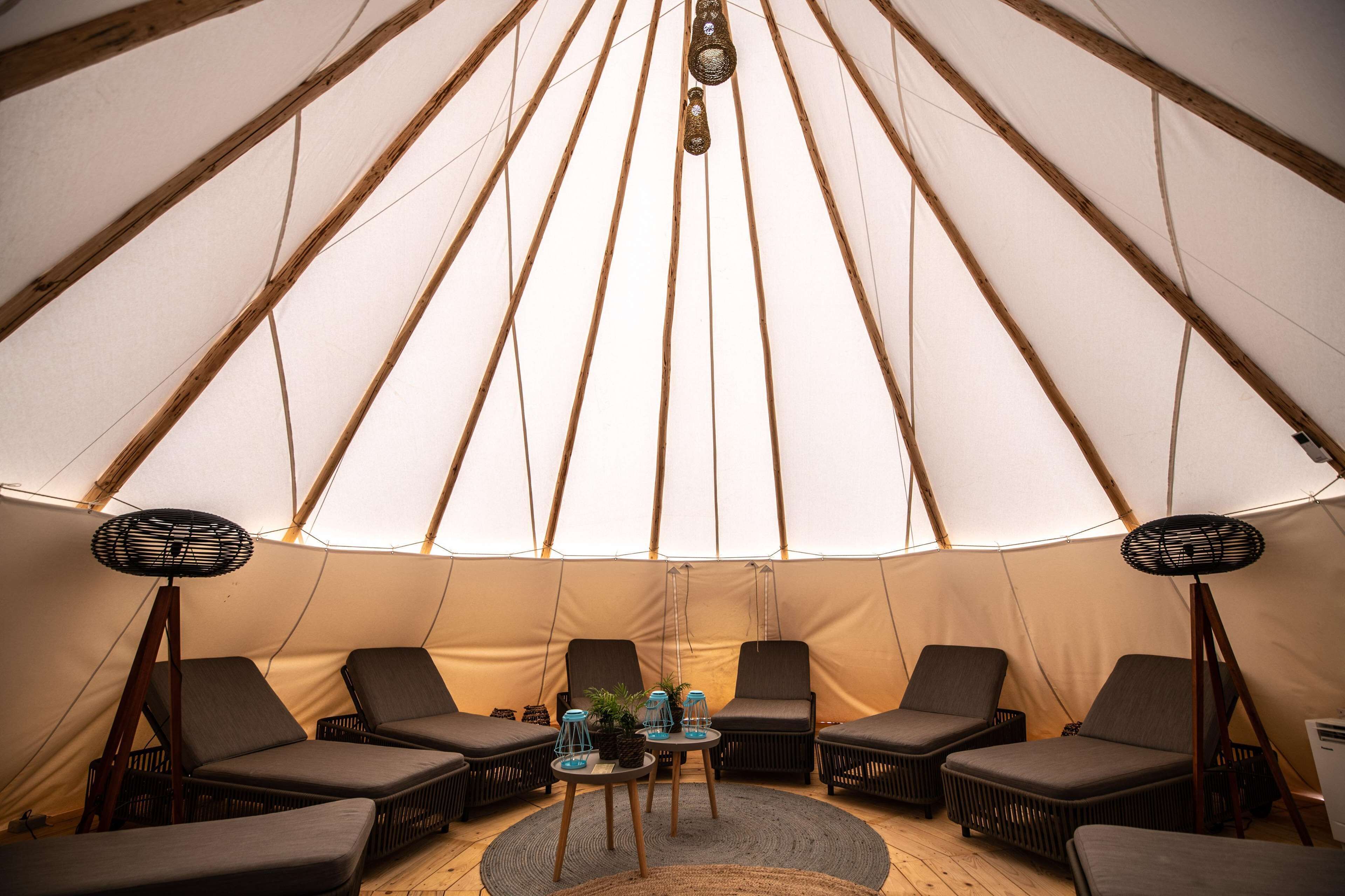 A large tent with a high ceiling and multiple seating areas, including lounge chairs and tables with drinks and plants.