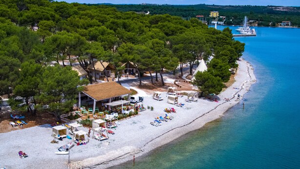 A beachside resort with a white sandy beach, a small dock with boats, and a cluster of buildings surrounded by trees. - Arena One 99 Glamping (Medulin)