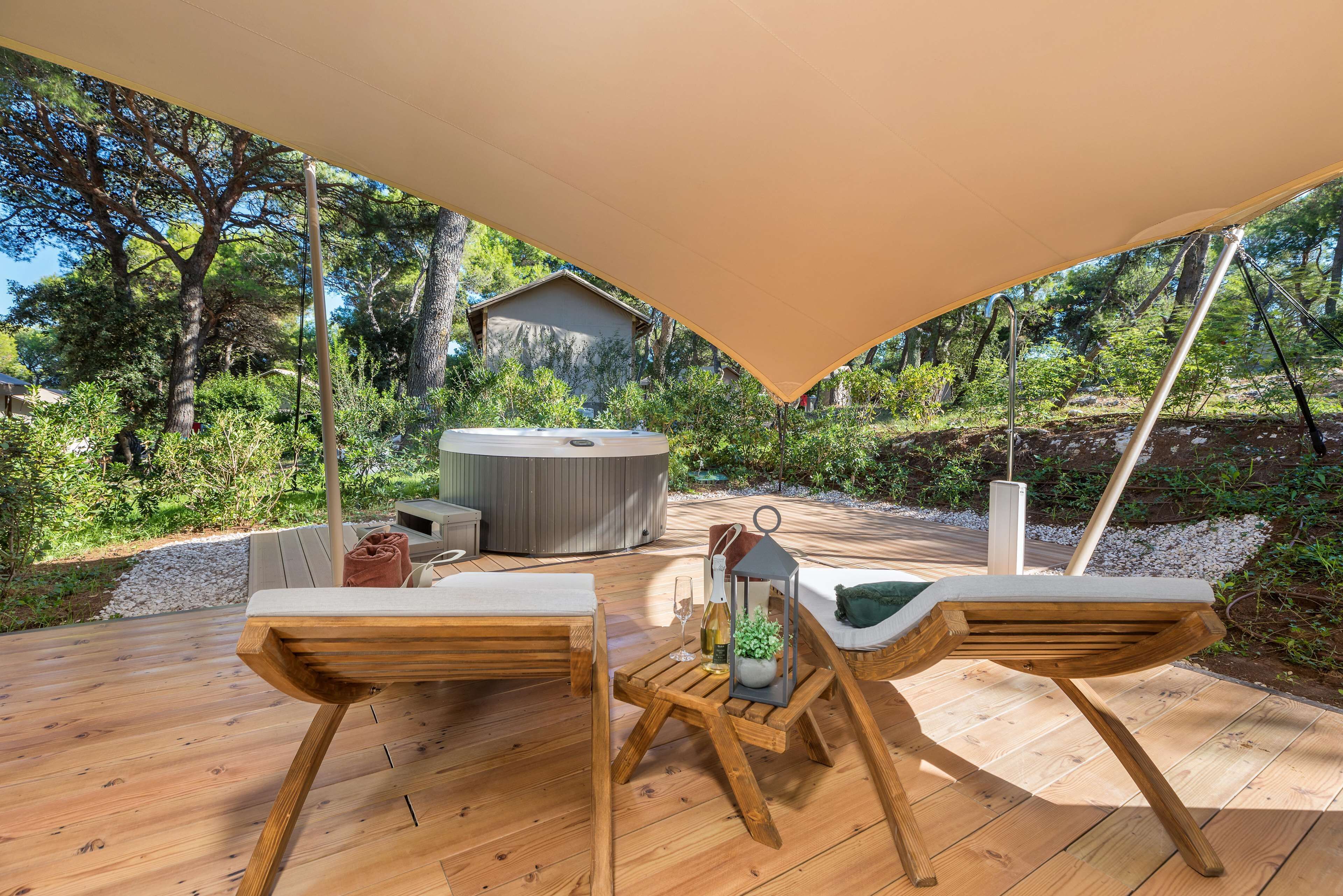 An outdoor deck with wooden furniture, a hot tub, and a canopy providing shade.
