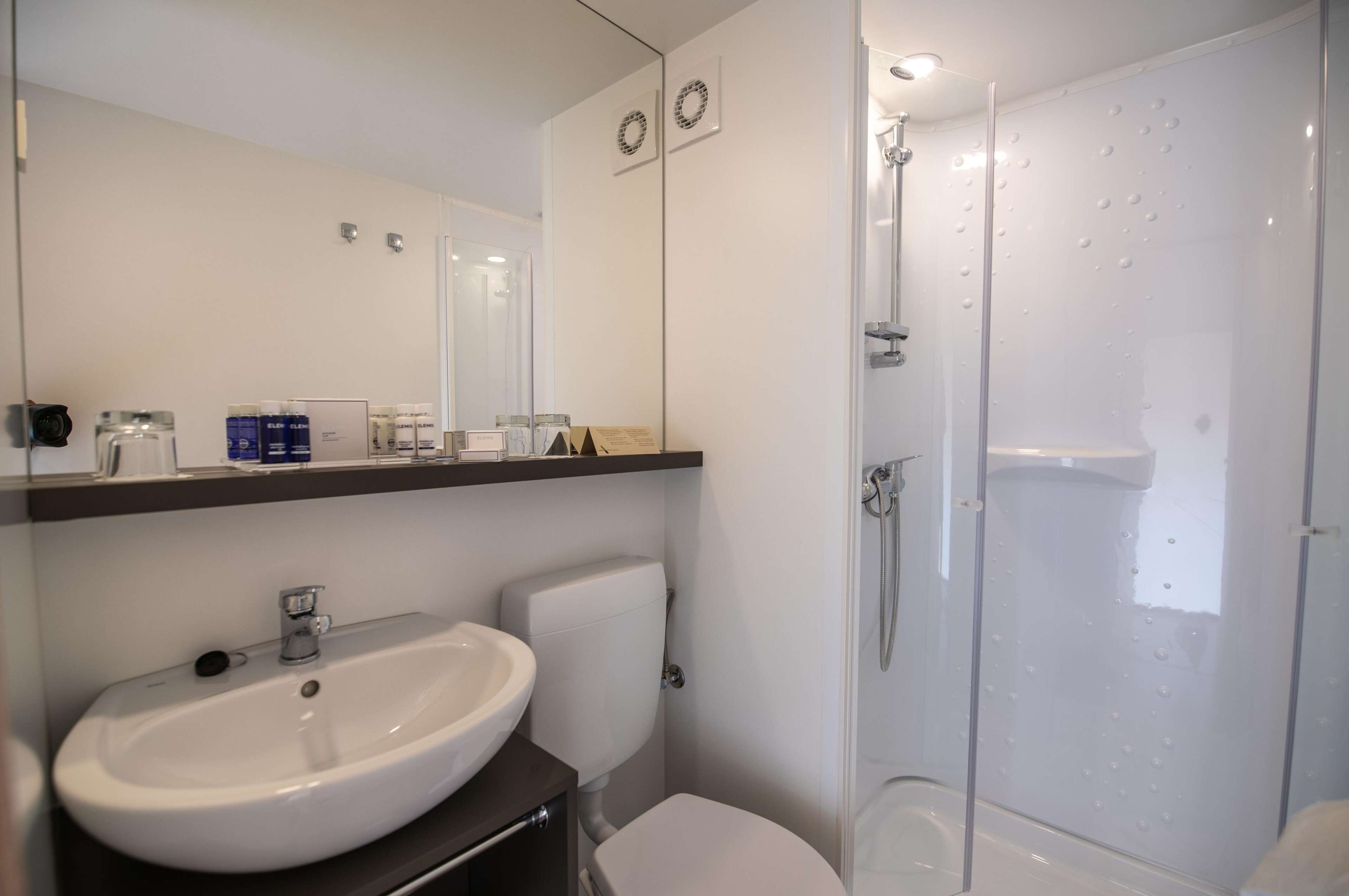 Et moderne badeværelse med hvid vask, toilet og brusekabine med glasvægge.