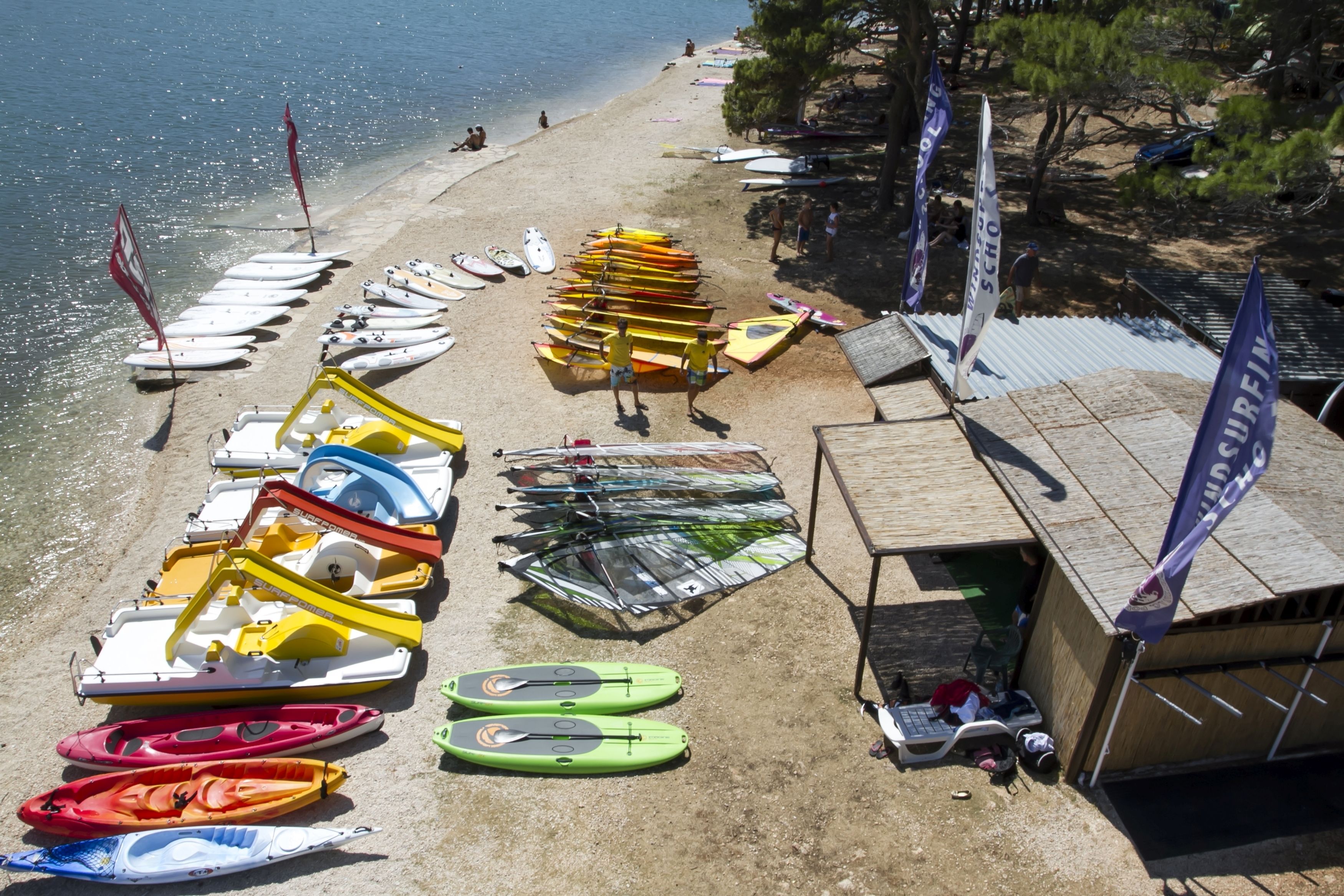 Een strand met tal van kajaks en kano's die in de branding liggen, een houten constructie en vlaggen.