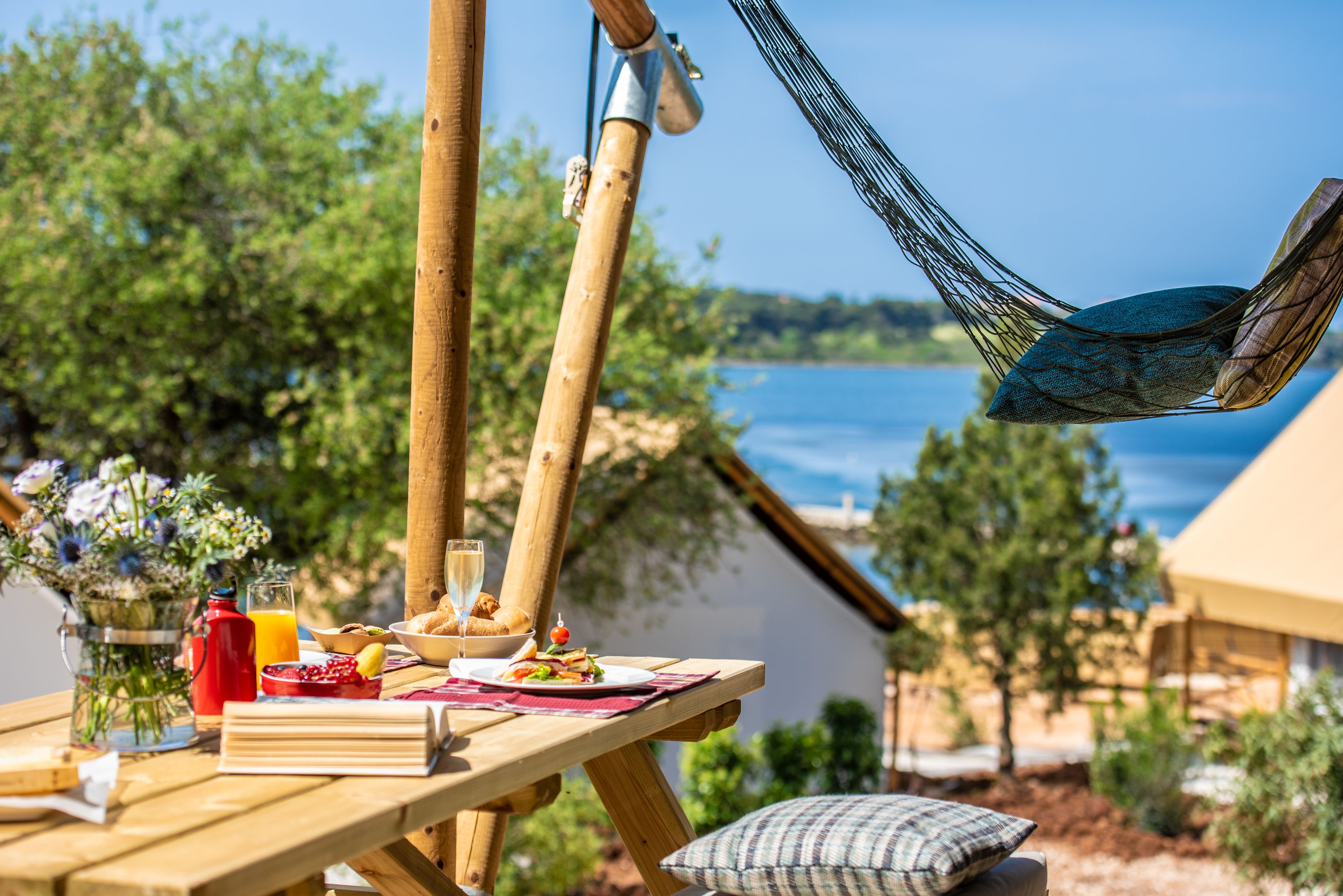 Una mesa de picnic de madera con comida, una hamaca y vistas al mar.