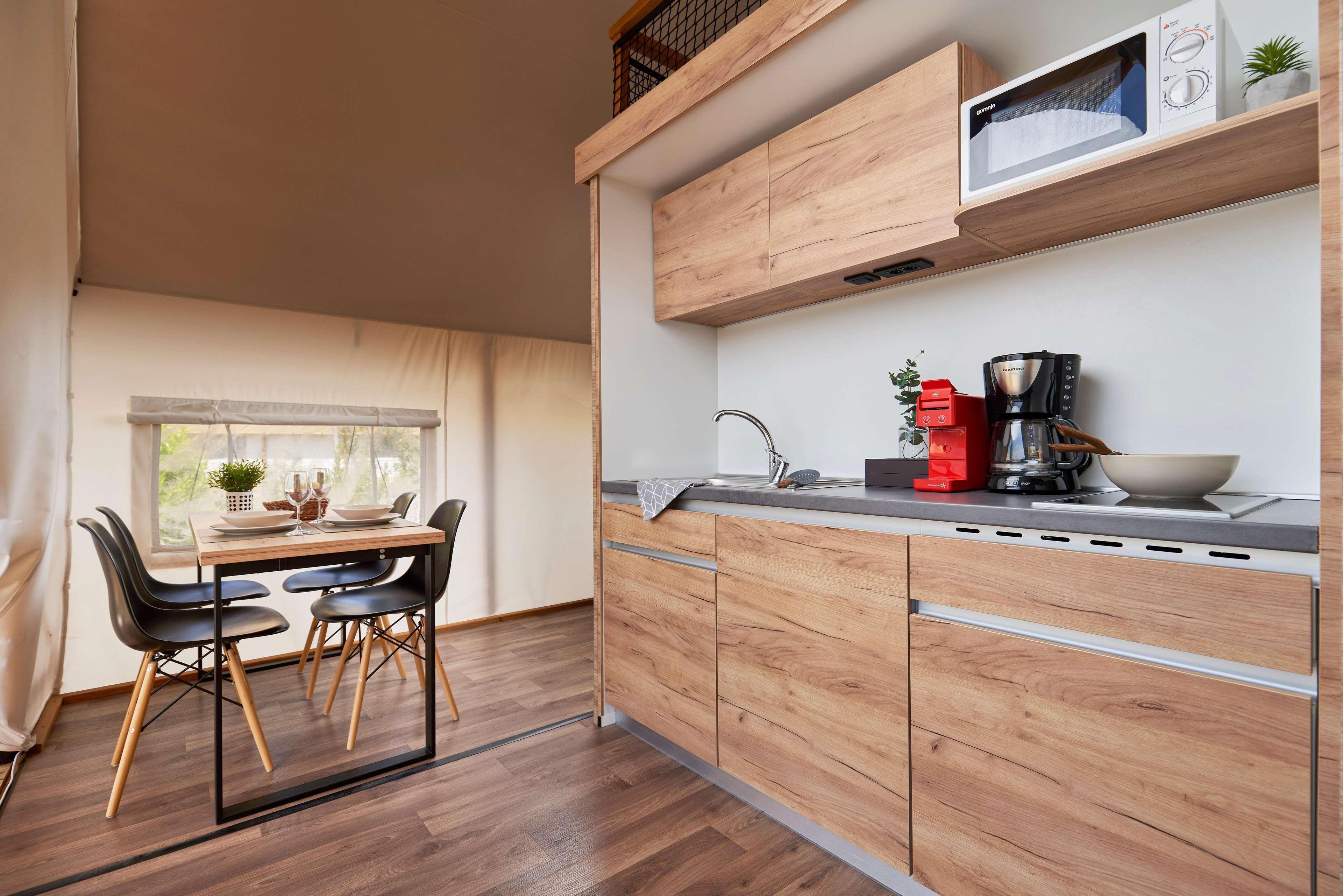 Eine moderne Küche mit Holzschränken, einer Mikrowelle, einer Kaffeemaschine und einem Essbereich mit Tisch und Stühlen.