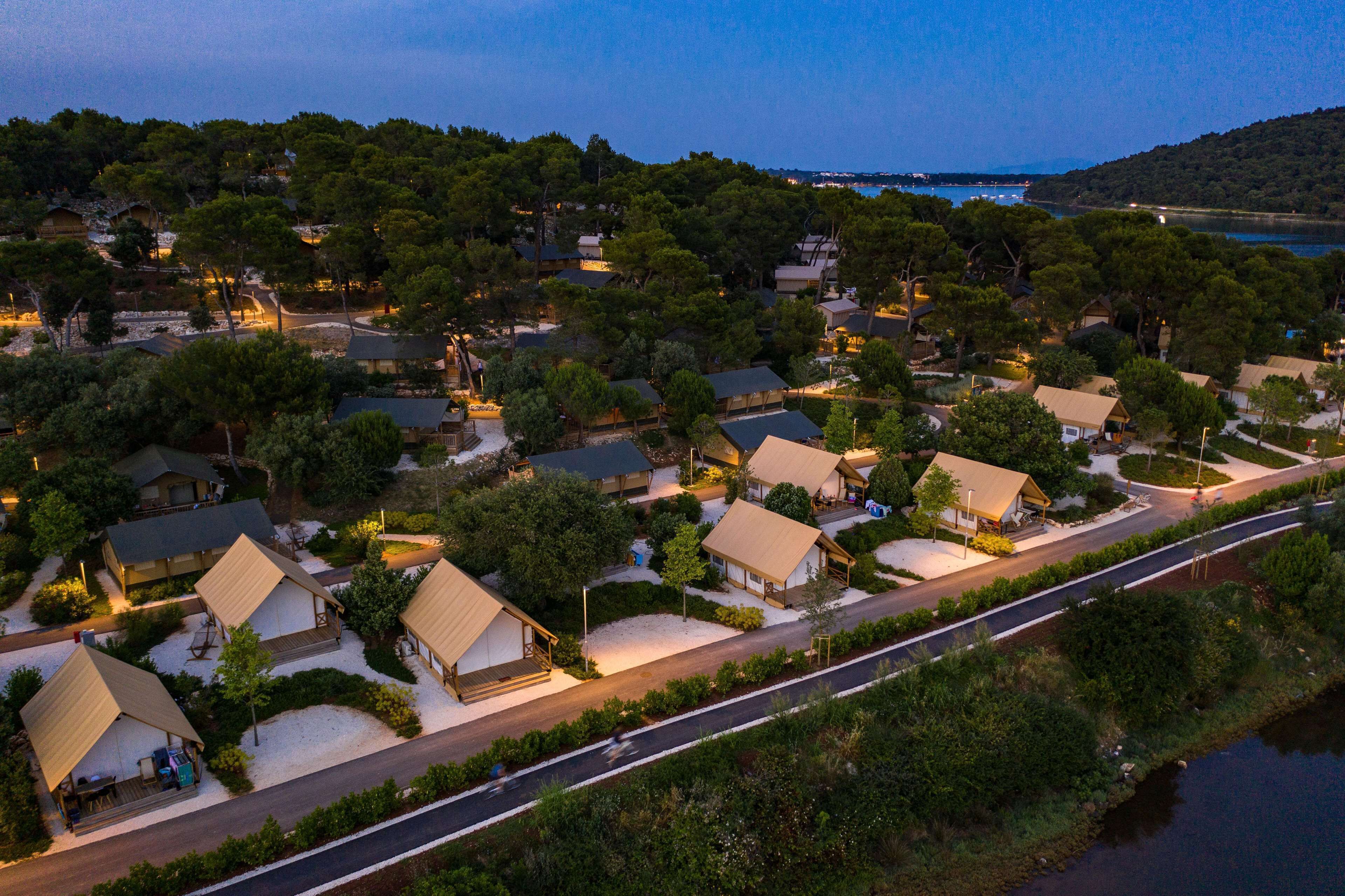 An aerial view of a resort with multiple bungalow-style accommodations, a main road, and a body of water in the background.