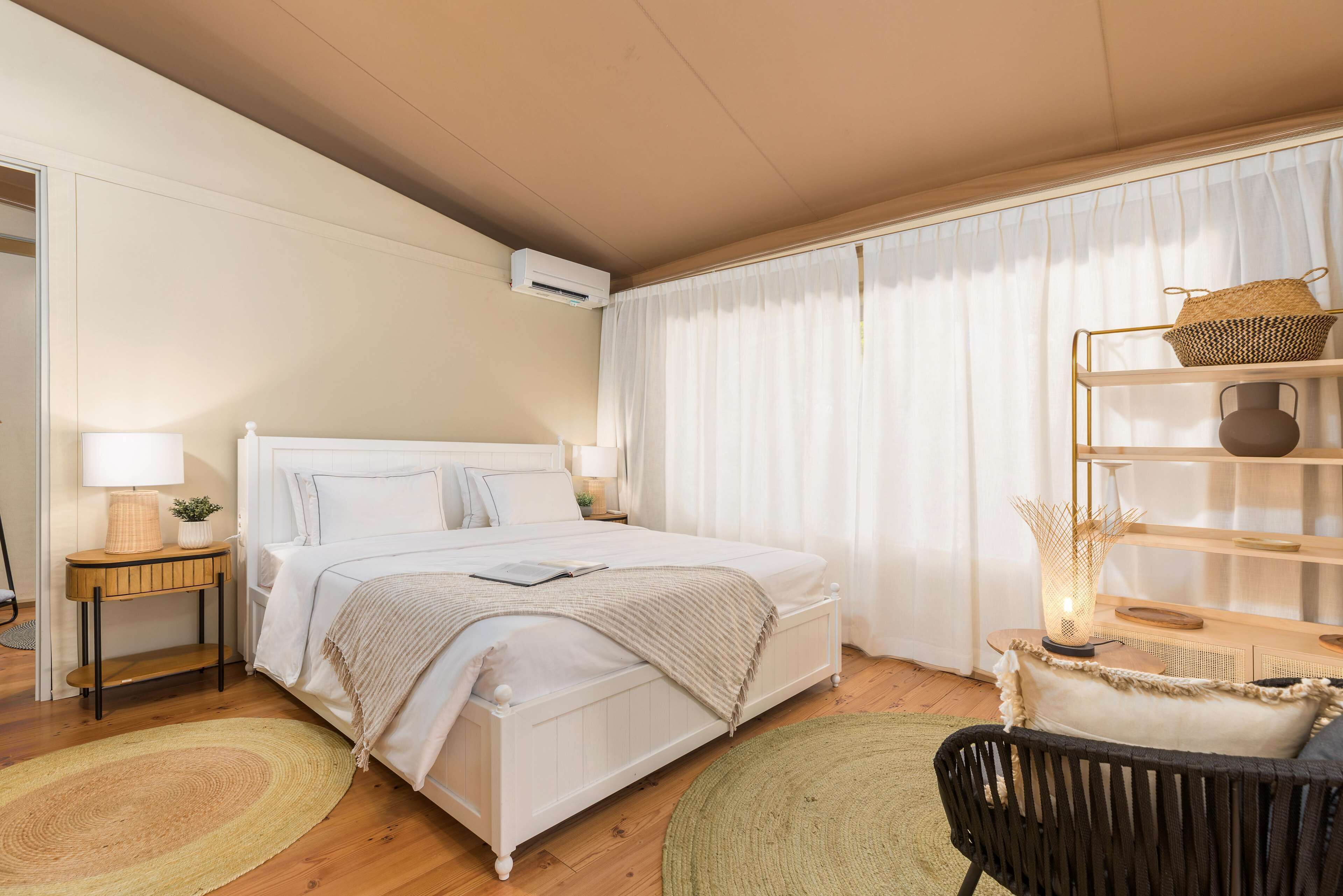 A neatly arranged bedroom with a bed, bedside tables, a lamp, and a shelf with decorative items.