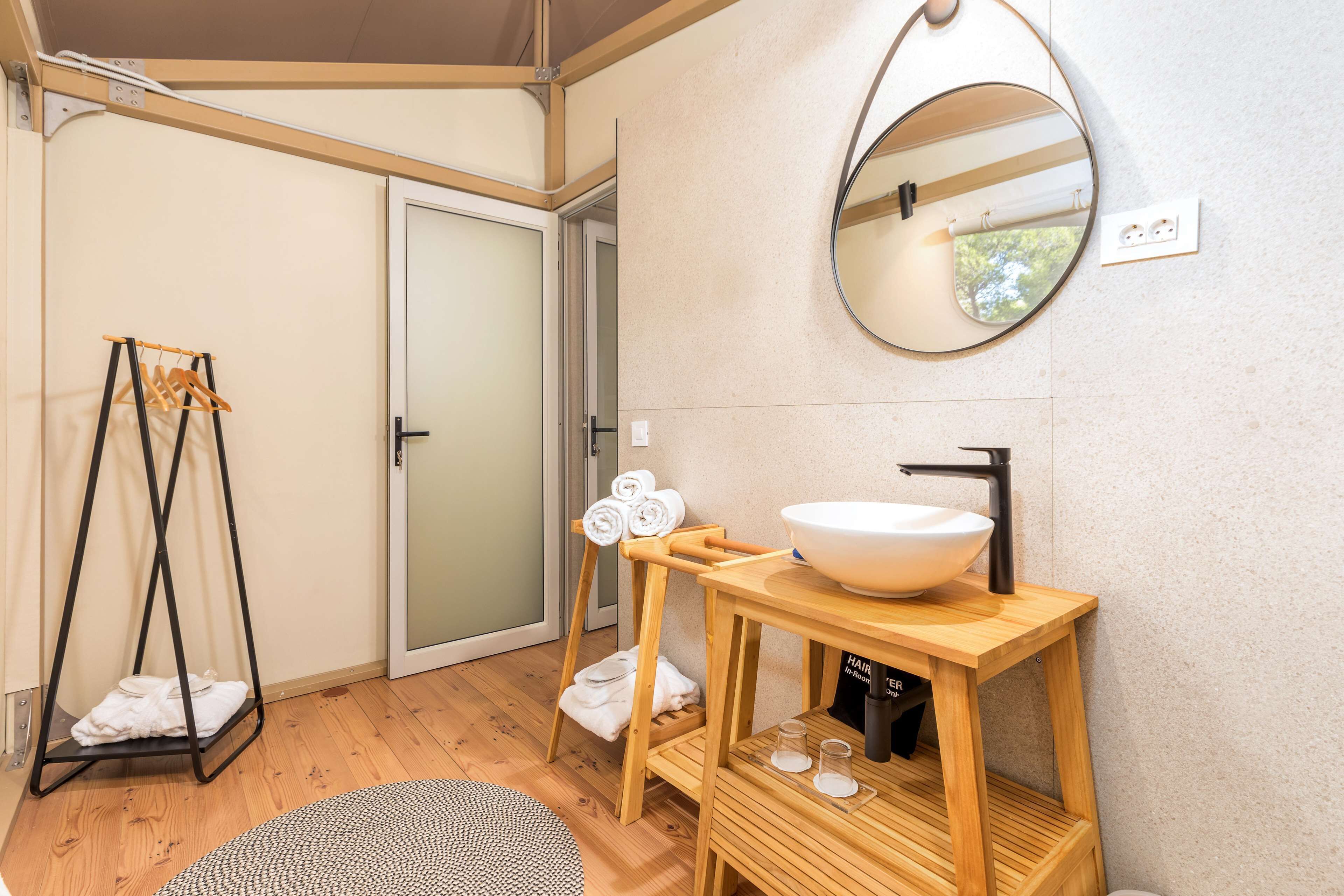 Ein Badezimmer mit einem Holzkosmetikschrank, einem runden Spiegel und einem Handtuchhalter.