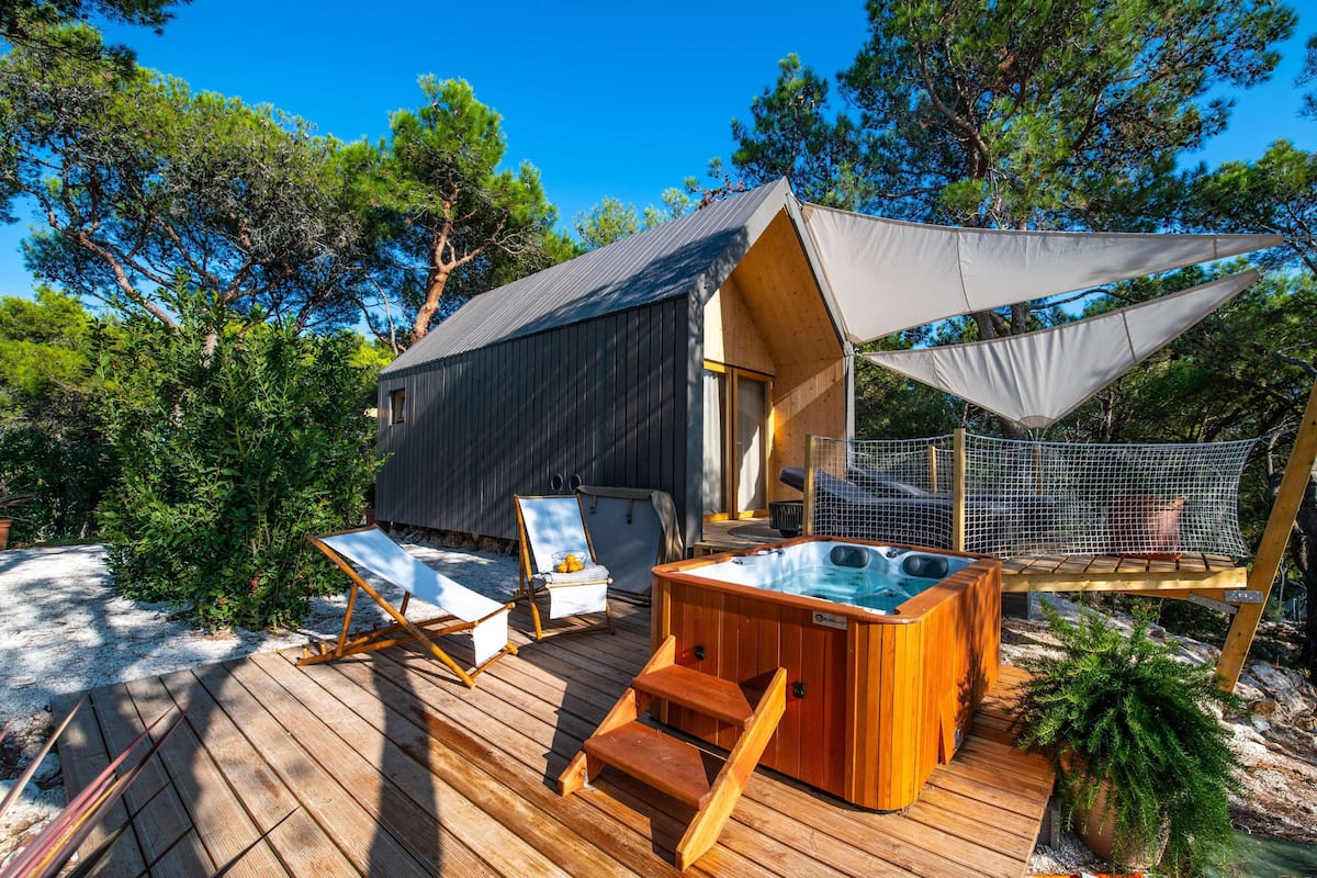 A wooden deck with a hot tub, lounge chairs, and a small building with a sloped roof.