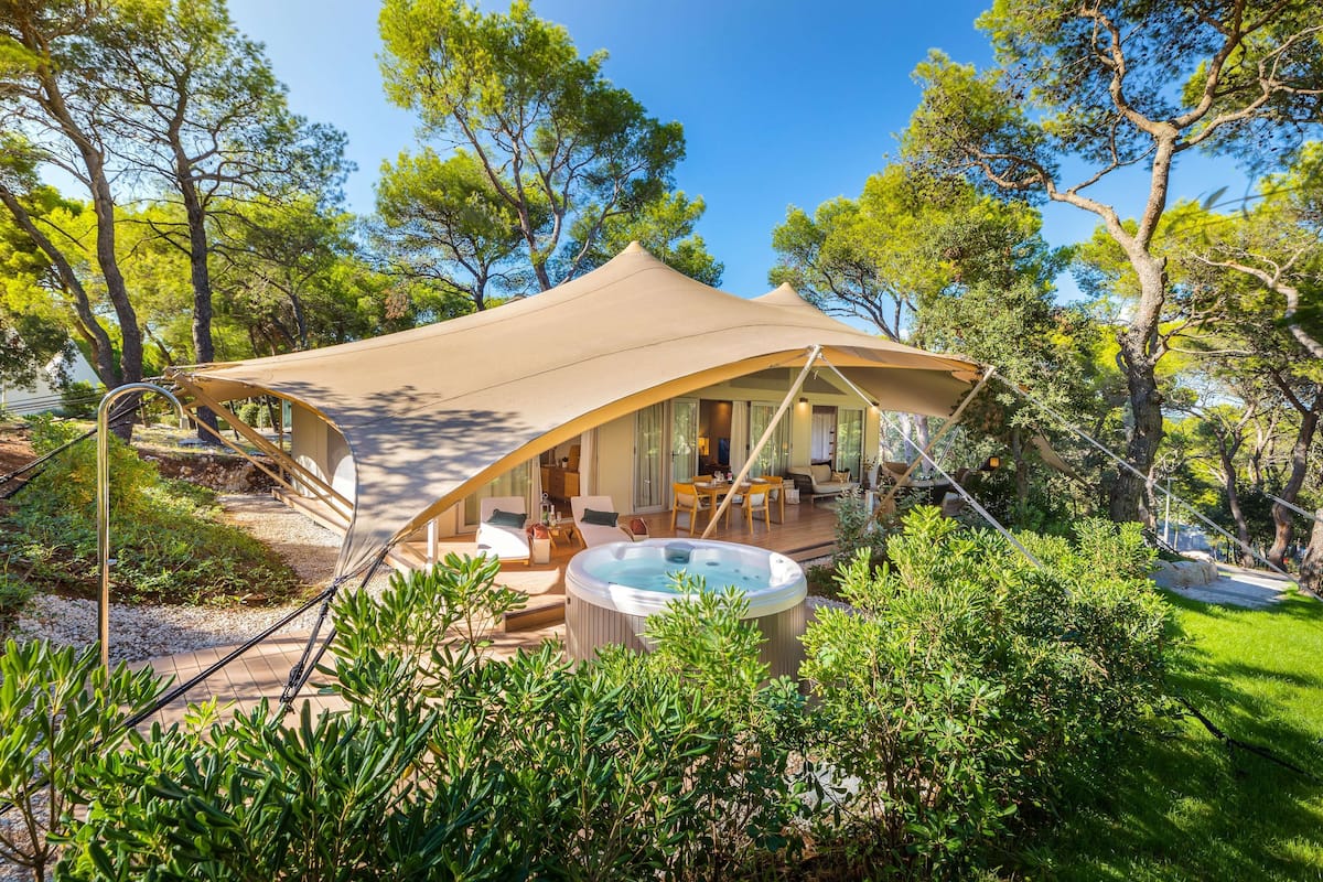 A luxurious outdoor hot tub area with a canopy, surrounded by lush greenery and trees.