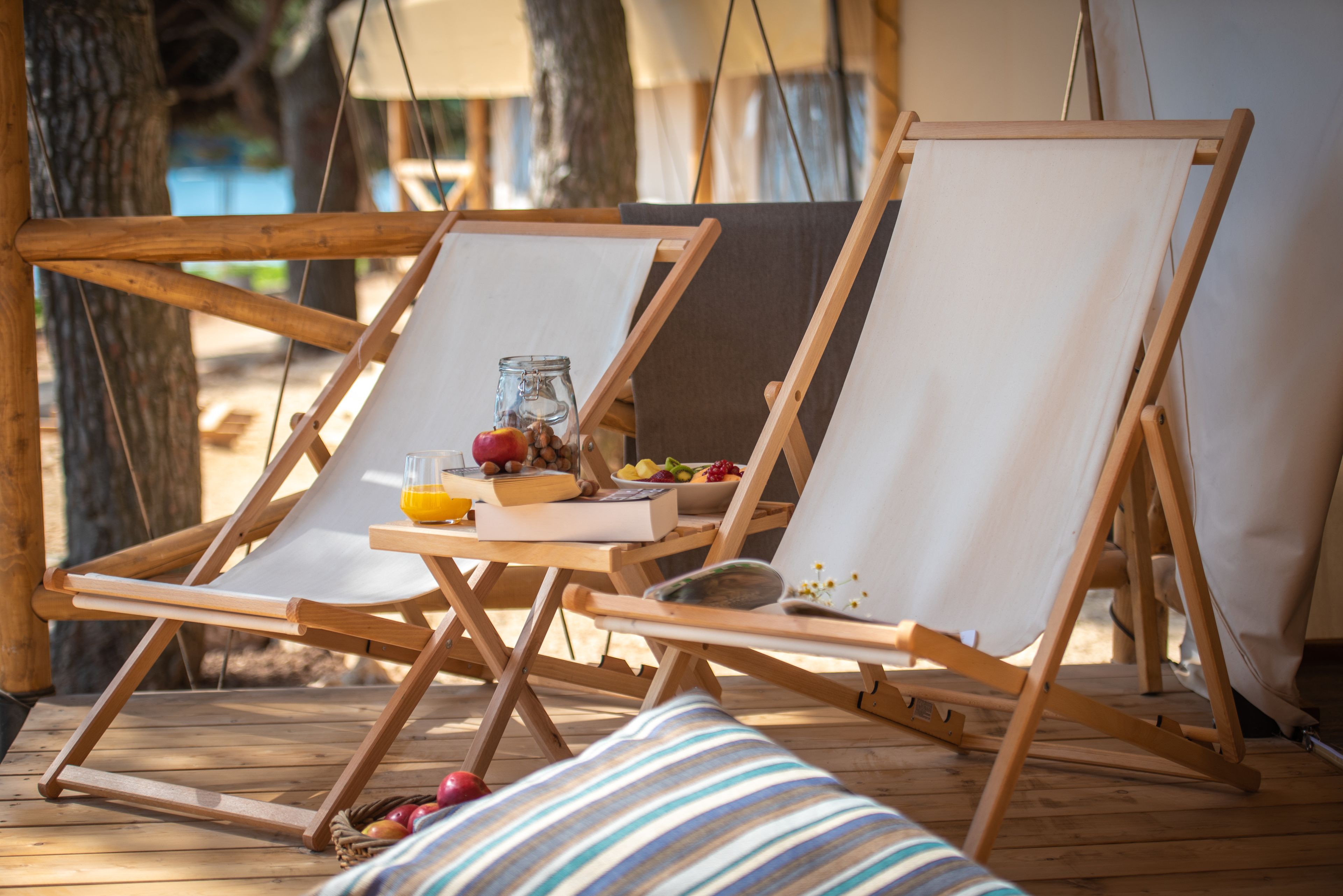 Een houten terras met twee canvas stoelen, een tafel met fruit, een glazen pot en een boek.
