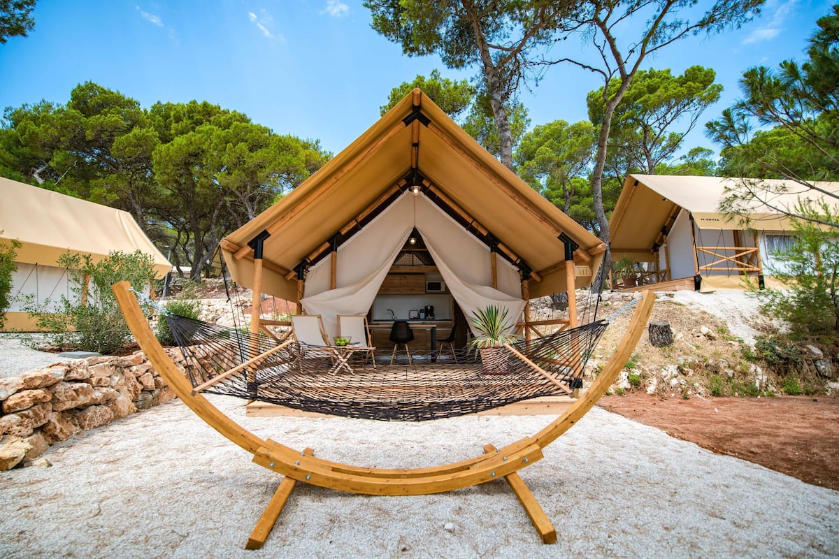 A cozy, single-room tent with a wooden frame and a thatched roof, surrounded by natural scenery and a hammock.