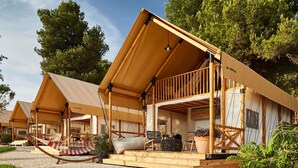 A series of wooden, AADRIA-branded tents with open sides, set on a gravel surface, surrounded by greenery. - Arena One 99 Glamping (Medulin)
