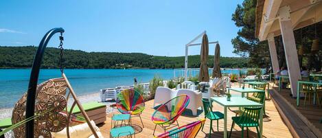 Une terrasse dotée de chaises, de tables et de parasols en osier, offrant une vue sur un lac.