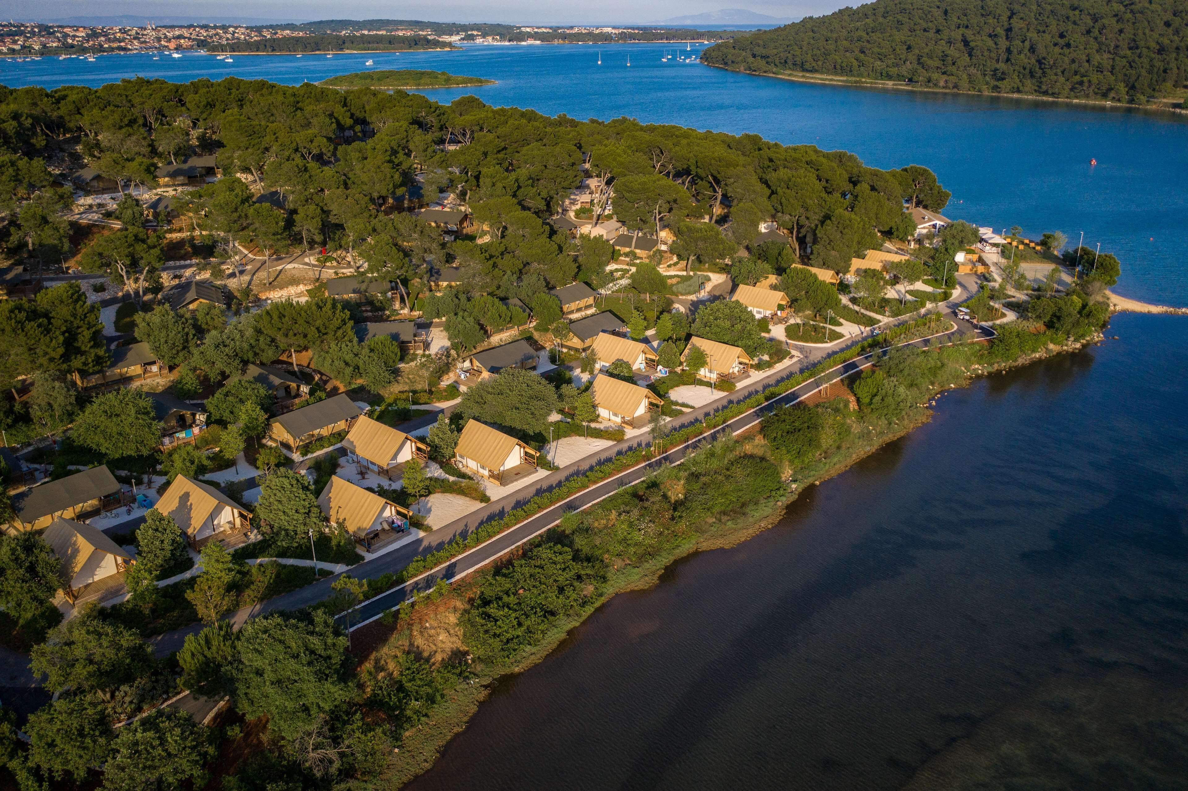 An aerial view of a coastal residential area with houses, a road, and a body of water.
