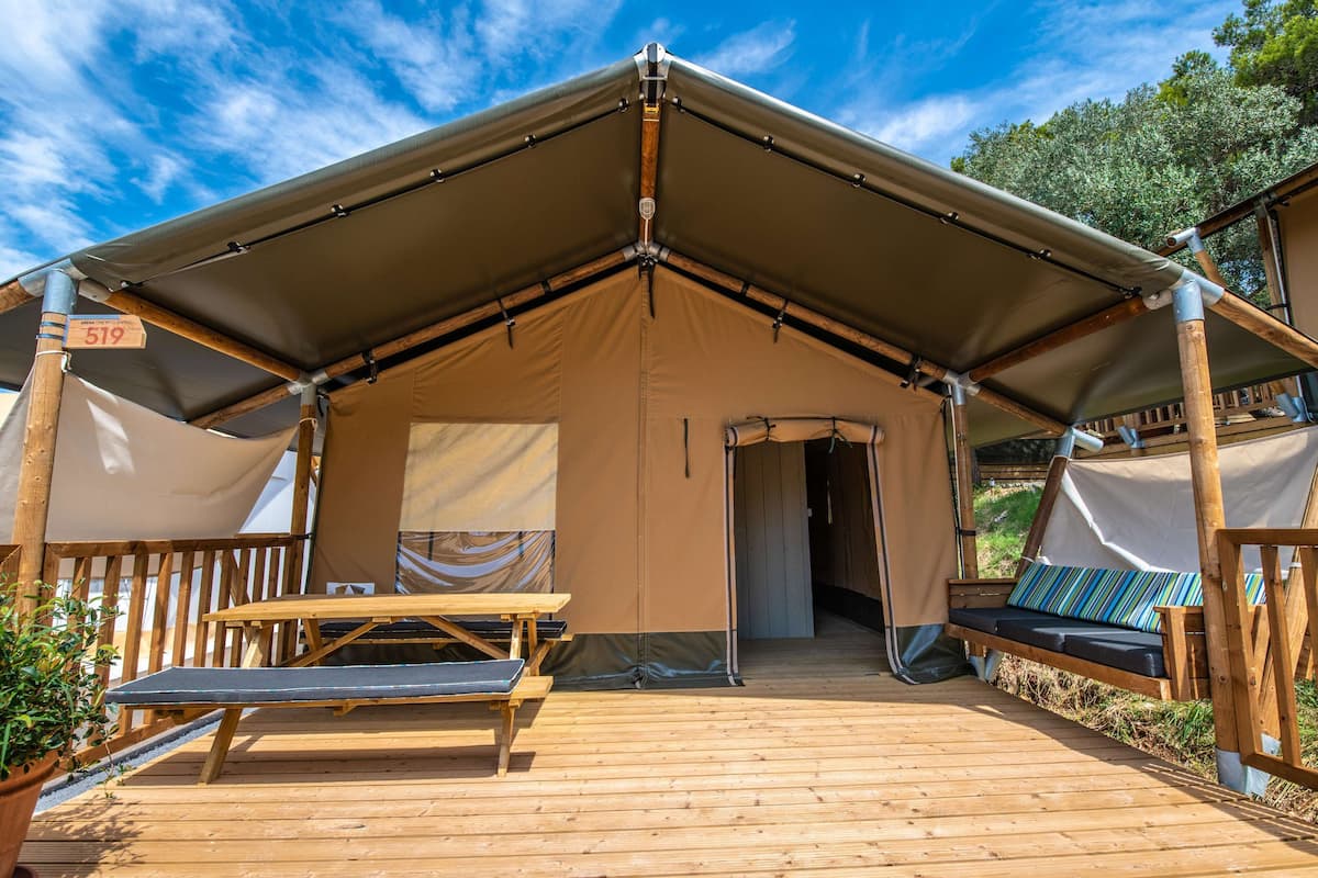 A tented accommodation with a wooden deck, a picnic table, and a bench with cushions.