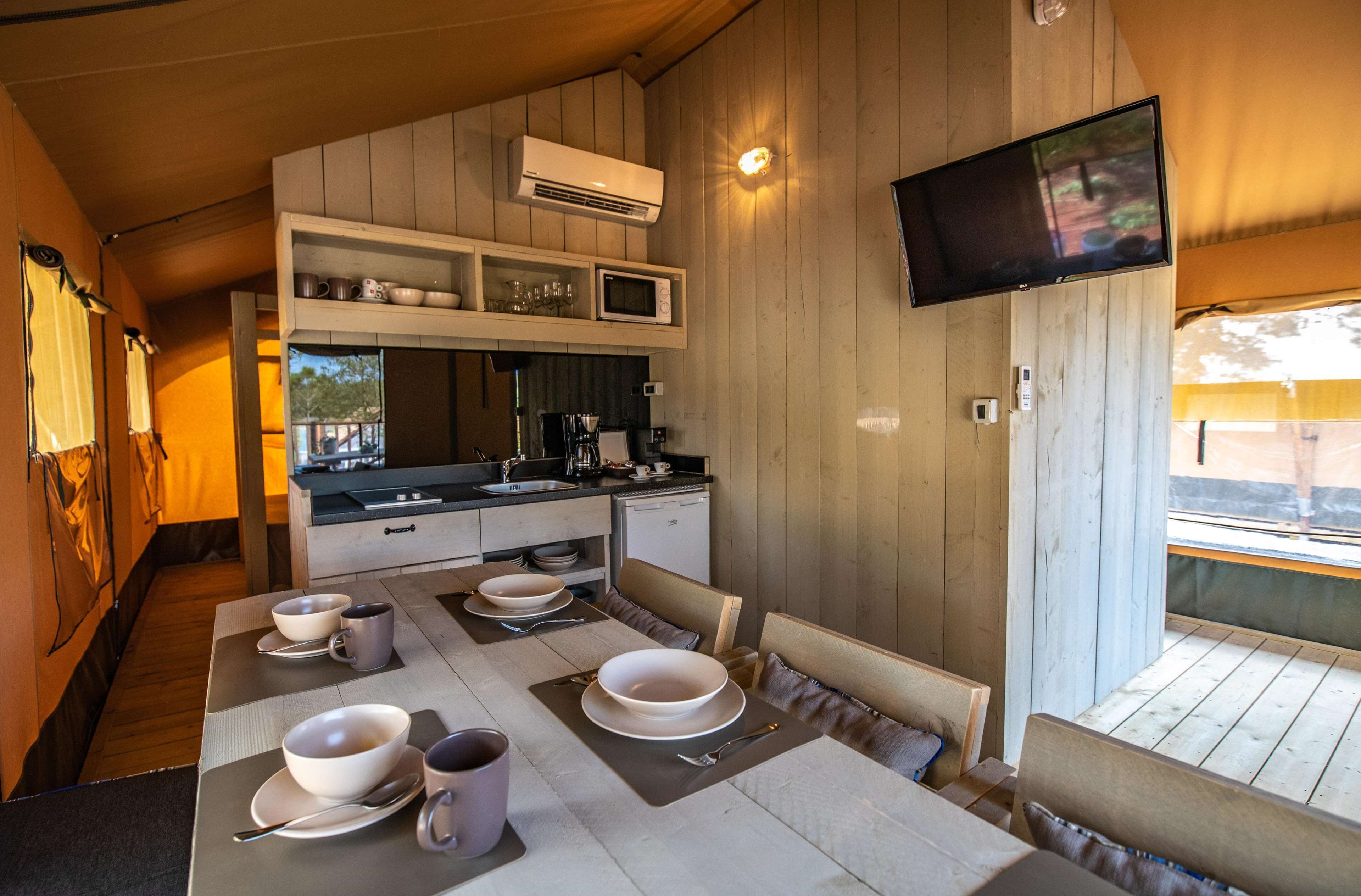 A compact kitchen with a dining area, a flat-screen TV mounted on the wall, and a view of the outdoors.