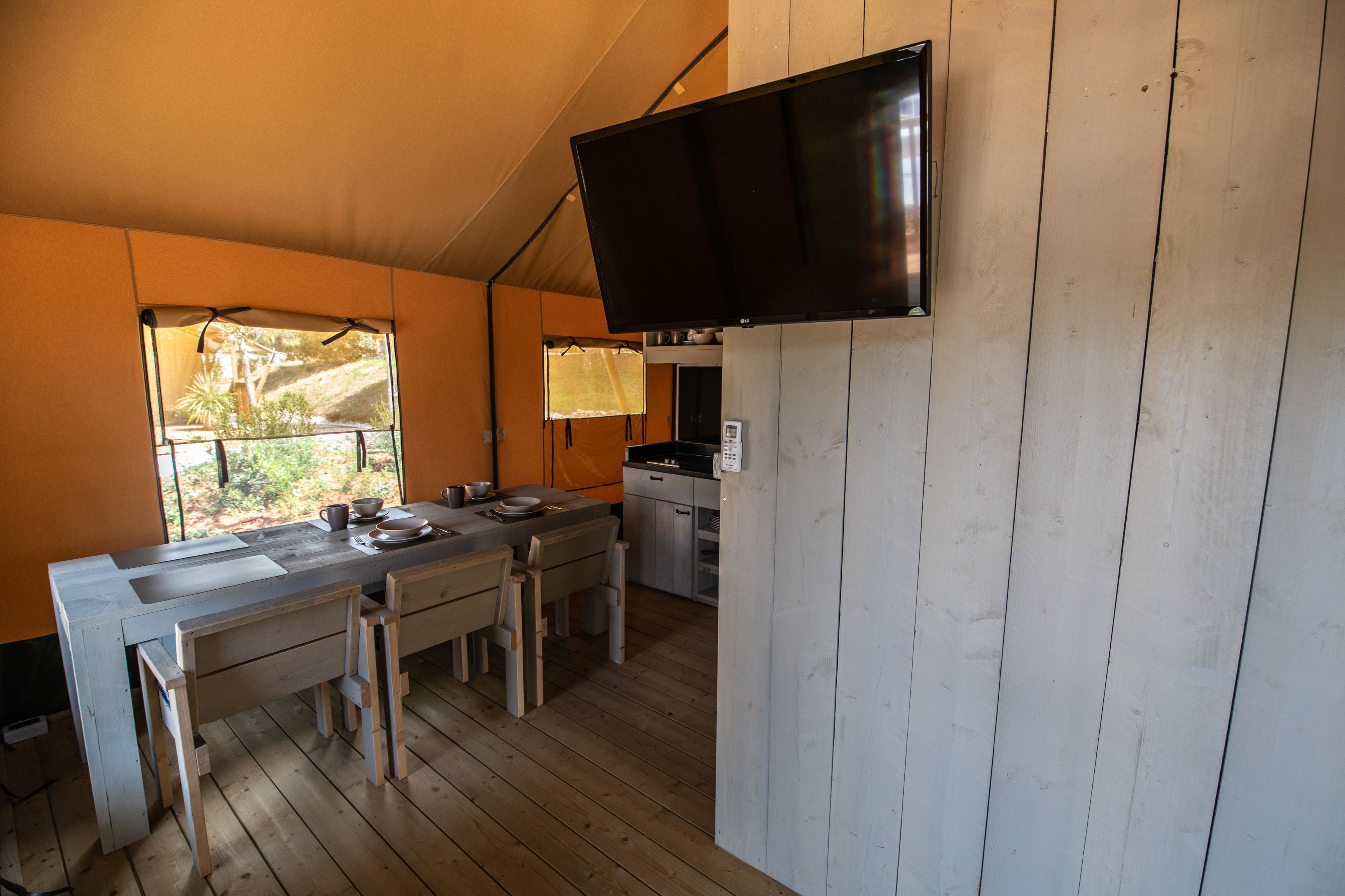 Une cuisine compacte avec des plans de travail en bois, une table à manger et des chaises. Un téléviseur à écran plat est fixé au mur.