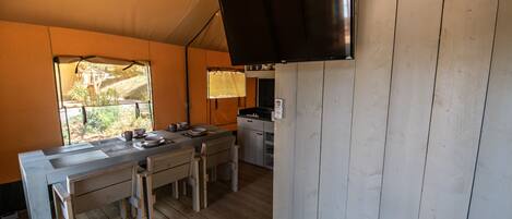 Une cuisine compacte avec des plans de travail en bois, une table à manger et des chaises. Un téléviseur à écran plat est fixé au mur.