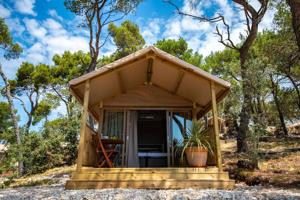 A small wooden cabin with a sloped roof, a sliding glass door entrance, and a small patio area with a table and chairs.
