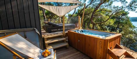 A wooden deck with a hot tub, a lounge chair, and a covered seating area with a netted table.