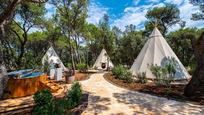 A pathway leading to a series of conical tents surrounded by trees, with a hot tub and a small structure nearby. - Arena One 99 Glamping (Medulin)